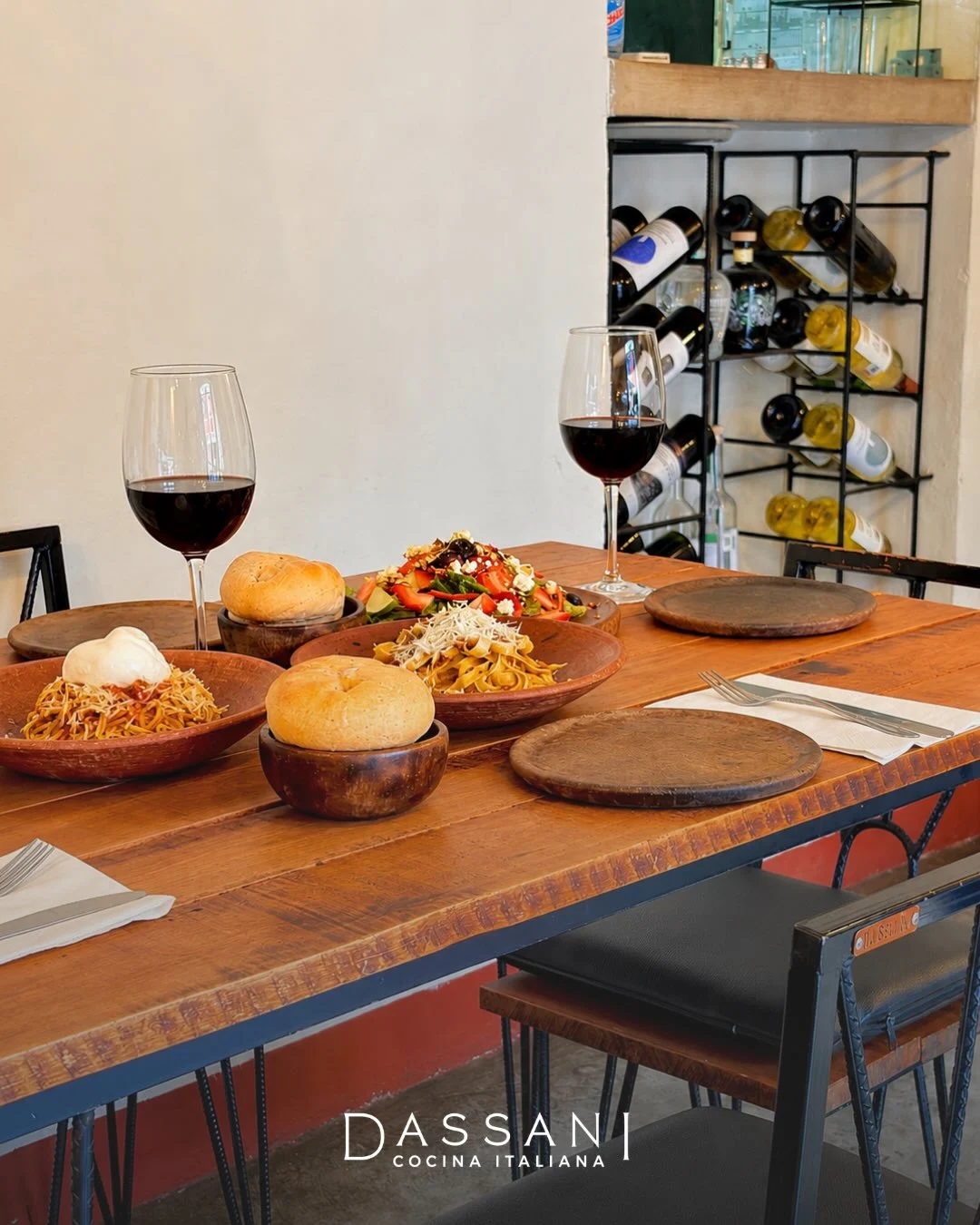 Mesa de Dassani con pastas, pan y dos copas de vino; al fondo, el botellero del comedor